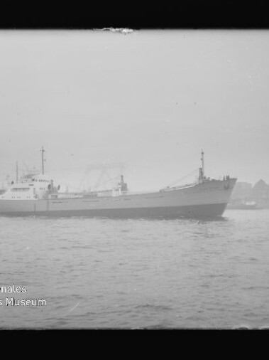 Schwarzweißaufnahme eines Frachtschiffs vor nebliger Hafenkulisse mit Kränen; Wasserzeichen Internationales Maritimes Museum Hamburg.