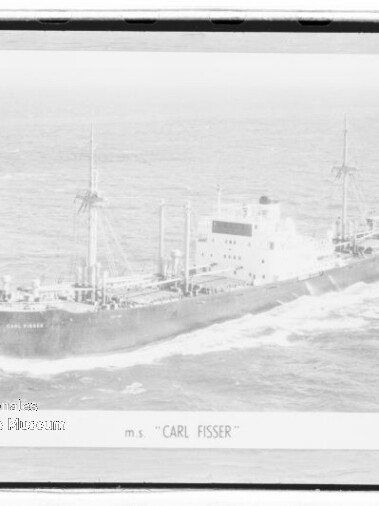 Schwarzweiß-Luftaufnahme des Frachtschiffs m.s. CARL FISSER mit zwei Masten, auf See fahrend und Bugwelle sichtbar.