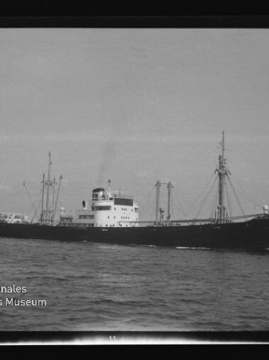 Schwarzweißaufnahme eines Frachtschiffs mit Ladekränen auf ruhiger See, mit Internationales Maritimes Museum Hamburg Wasserzeichen links unten.