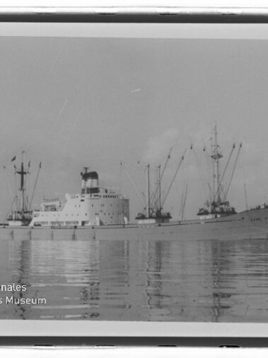 Frachtschiff mit Kränen und Masten auf ruhigem Wasser, Schwarzweißfoto mit Wasserzeichen des Maritimen Museums Hamburg.