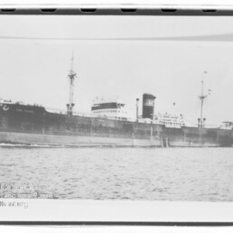 Großes Frachtschiff mit schwarzem Rumpf, zwei Masten und markantem Schornstein fährt ruhig über das Meer