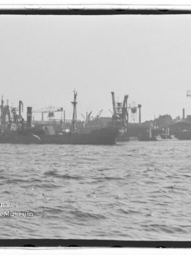 Frachtschiffe und Kräne in einem Industriehafen, Wellengang im Vordergrund, Wasserzeichen 