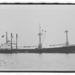 Schwarzweiß-Seitenansicht eines Frachtschiffs mit Ladebäumen und Masten auf ruhiger See; Wasserzeichen des Maritimen Museums Hamburg