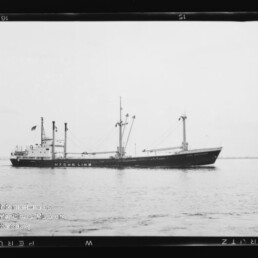 Schwarzweißaufnahme eines Frachtschiffs mit der Aufschrift HYCER LINE, Masten und Ladekränen, ruhig auf dem Meer vor flachem Horizont.