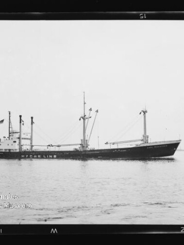 Schwarzweißaufnahme eines Frachtschiffs mit der Aufschrift HYCER LINE, Masten und Ladekränen, ruhig auf dem Meer vor flachem Horizont.