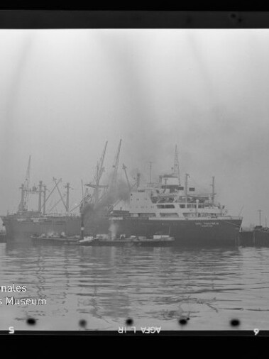 Frachtschiff am Kai mit Kränen, Rauch über dem Schiff und Spiegelung im Wasser; Schriftzug Maritimes Museum Hamburg sichtbar.
