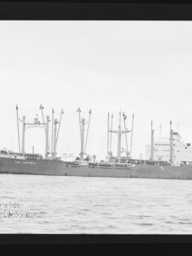 Frachtschiff mit mehreren Ladekränen und Masten auf ruhiger See in schwarzweiß.