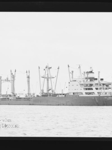 Frachtschiff mit mehreren Ladekränen und Aufbauten in ruhiger See, schwarzweißes Foto mit Museumslogo unten links.