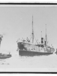 Großes Dampfschiff neben Schlepper auf ruhigem Wasser; historisches Schwarzweiß-Foto.