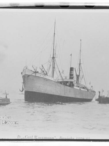 Schwarzweißaufnahme des Dampfschiffs „D. v. Carl Woermann“ mit hohem Schornstein und Masten, begleitet von einem Schlepper im Hafen.