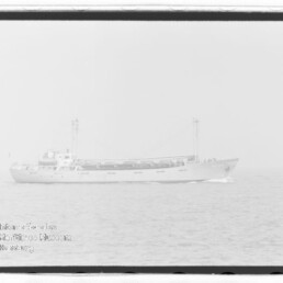 Frachtschiff mit zwei Masten auf ruhiger See, schwaches Wasserzeichen unten links.