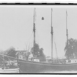 Dreimastiger Segler am Ufer mit kleinem Beiboot, Bäume und Haus im Hintergrund und Museumsstempel unten links.