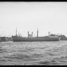 Frachtschiff mit Aufschrift Hamburg-Chicago Linie liegt im Hafen vor Kränen, Wasser im Vordergrund
