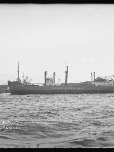 Frachtschiff mit Aufschrift Hamburg-Chicago Linie liegt im Hafen vor Kränen, Wasser im Vordergrund