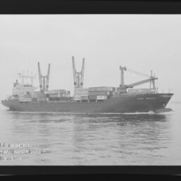 Containerschiff mit Containern und Deckkränen fährt über ruhiges Wasser; Wasserzeichen: Maritimes Museum Hamburg