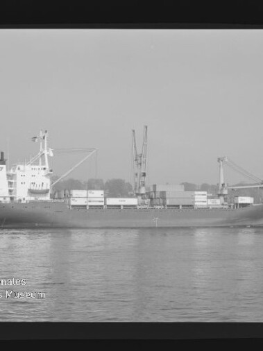 Frachtschiff mit Containern und zwei Ladekränen fährt auf ruhigem Wasser vor Uferkulisse; Museumslogo unten links.
