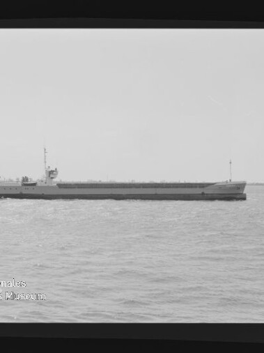 Langgestrecktes Frachtschiff mit Aufbauten achtern auf ruhiger See; Schwarzweißfoto mit Wasserzeichen 'Int. Maritimes Museum'