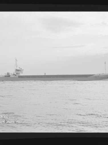 Langgestrecktes Frachtschiff mit niedrigem Aufbau auf ruhiger See unter hellem Himmel, schwarzweißes Foto.