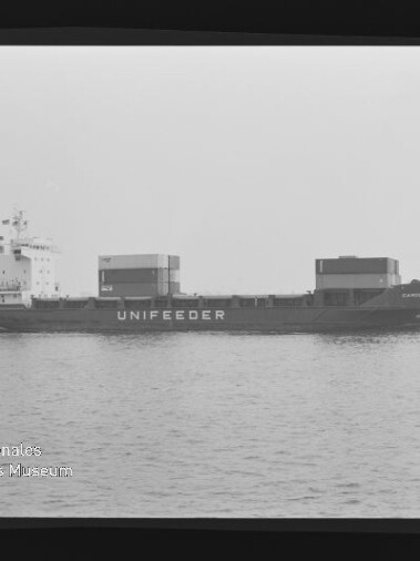 Schwarzweiß-Seitenansicht eines Frachtschiffs mit der Aufschrift UNIFEEDER und Containeraufbauten, ruhig auf See mit sichtbarem Filmrand.