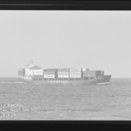 Frachtschiff UNIFEEDER mit gestapelten Containern fährt auf ruhiger See, Horizont und leichter Wellengang sichtbar.