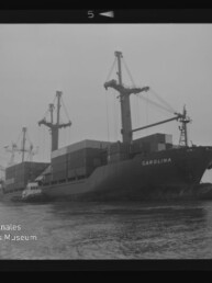 Frachtschiff CAROLINA mit Containern und Ladekränen, begleitet vom Schlepper, auf nebligem Wasser; Museumslogo unten links.