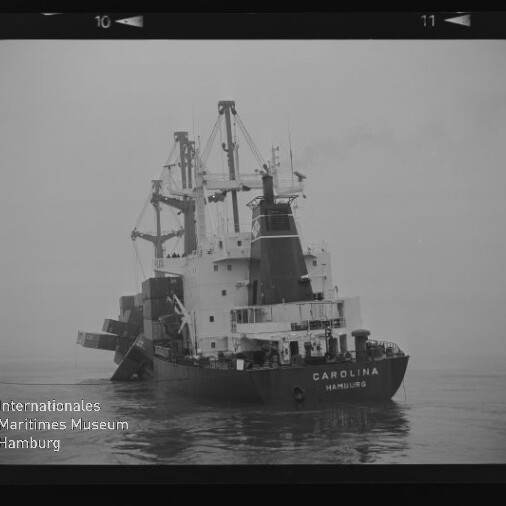 Schwarzweiß-Foto eines Frachtschiffs CAROLINA (Hamburg) mit Ladekränen auf ruhiger See.