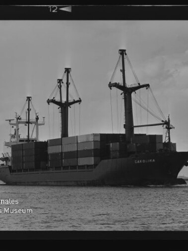 Containerschiff CAROLINA mit gestapelten Containern und Ladekränen auf ruhigem Hafenwasser im schwarzweiß-Filmrahmen.