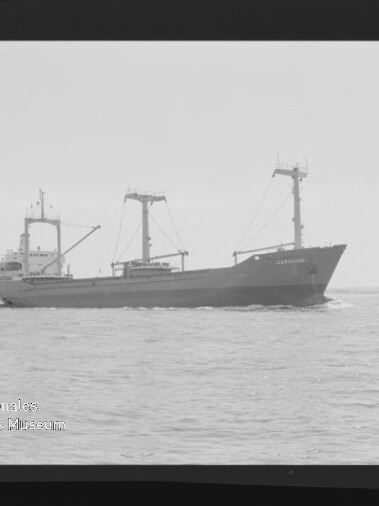 Schwarzweißaufnahme eines Frachtschiffs mit Ladebäumen auf ruhiger See, mit Filmrand (Kodak) und Museumswasserzeichen.
