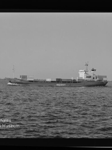 Frachtschiff mit gestapelten Containern quer zur Kamera auf ruhiger See vor flachem Horizont.