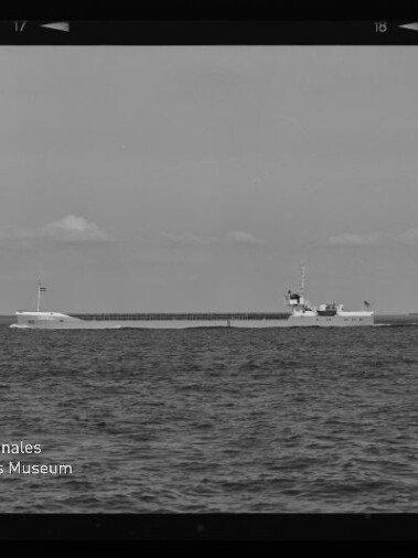 Schwarzweißaufnahme eines langen Frachtschiffs auf ruhiger See am Horizont mit niedrigen Wolken und Wasserzeichen Internationales Maritimes Museum Hamburg.