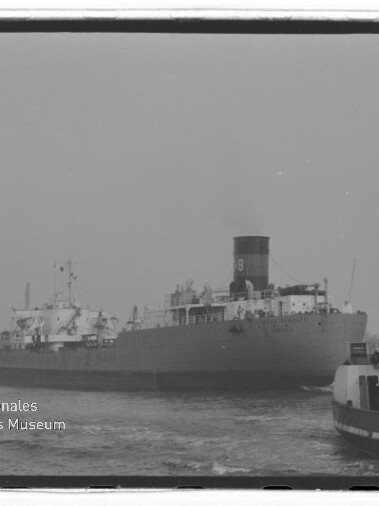 Großes Frachtschiff mit markantem Schornstein und Schlepper im Vordergrund, Wasserzeichen des Maritimen Museums Hamburg.