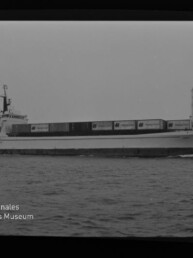 Seitenansicht eines Containerschiffs mit gestapelten Containern auf ruhiger See, Museumssignet unten links.