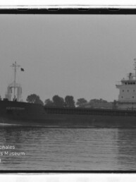Frachtschiff A.A. Amsterdam auf ruhigem Wasser vor baumbestandener Uferlinie, Schwarzweißfoto