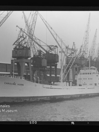 Frachtschiff CAROLINE HORN liegt am Industriequai vor einer Reihe großer Hafenkräne, schwarzweiß.