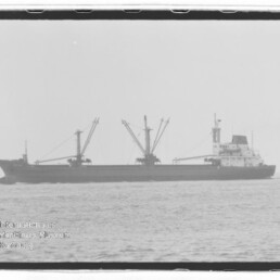 Frachtschiff mit drei Ladekränen auf ruhiger See, schwarzweißfoto mit Wasserzeichen Internationales Maritimes Museum Hamburg.