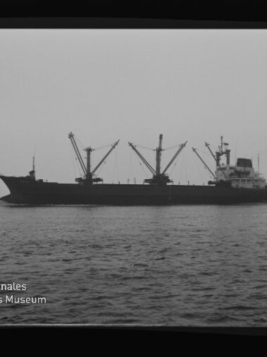 Frachtschiff mit mehreren Ladekränen in Seitenansicht auf ruhiger See, Schwarzweißaufnahme mit Museumslogo.