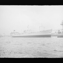 Großes weißes Passagierschiff längsseits im Hafen vor Kränen, ruhige See und Museum-Wasserzeichen links unten.