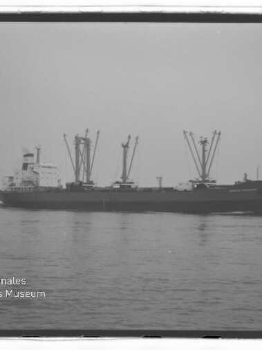 Frachtschiff mit mehreren Deckskränen auf ruhiger See, Schwarzweißaufnahme mit Wasserzeichen Internationales Maritimes Museum Hamburg.