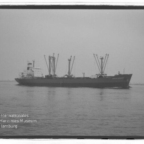 Frachtschiff mit mehreren Deckskränen auf ruhiger See, Schwarzweißaufnahme mit Wasserzeichen Internationales Maritimes Museum Hamburg.