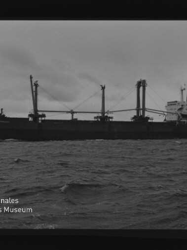 Schwarzweißfoto eines Frachtschiffs mit Ladekränen auf bewegter See; sichtbarer Wasserzeichentext Internationales Maritimes Museum Hamburg
