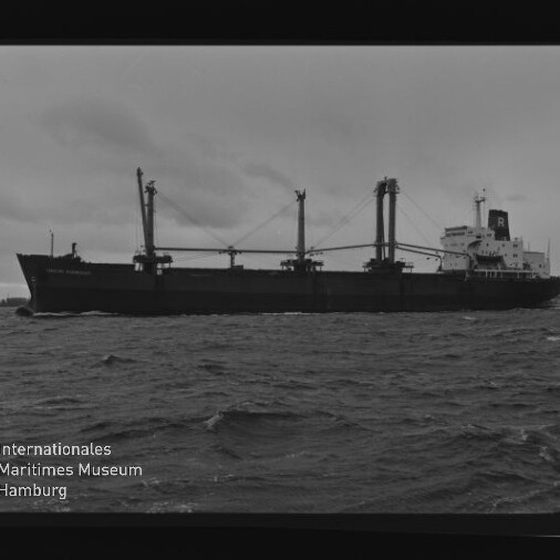 Schwarzweißfoto eines Frachtschiffs mit Ladekränen auf bewegter See; sichtbarer Wasserzeichentext Internationales Maritimes Museum Hamburg