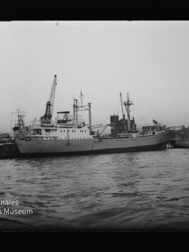 Frachtschiff am Kai in einem Hafen mit Kränen, schwarz-weiße Aufnahme mit Museumssignet des Maritimen Museums Hamburg.