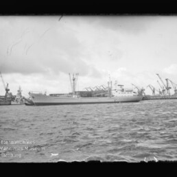Frachtschiff im Hafen vor Kranen, Wellengang im Vordergrund und Museumswasserzeichen Internationales Maritimes Museum Hamburg