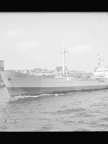 Frachtschiff Capricornus fährt in Hafennähe vor Lagerhäusern, mit leichter Bugwelle und Wasserzeichen Internationales Maritimes Museum Hamburg links unten