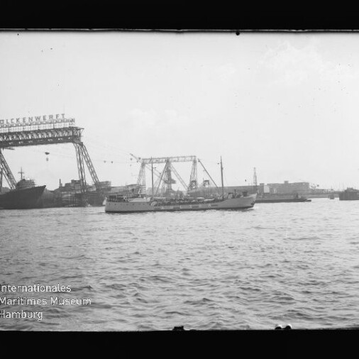 Kleines Handelsschiff im Hafen vor großen Werftkränen mit dem Schriftzug Stülckenwerft