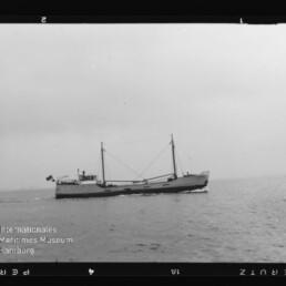 Kleiner Frachter mit zwei Masten auf ruhiger See unter bedecktem Himmel; Wasserzeichen Internationales Maritimes Museum Hamburg
