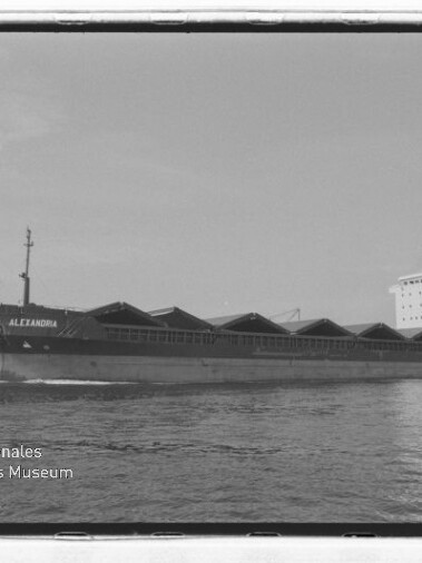 Frachtschiff ALEXANDRIA in Schwarzweiß mit spitzen Ladeluken auf ruhigem Wasser, Museumsstempel links unten