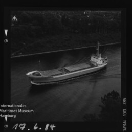 Schwarzweiß-Luftaufnahme eines Frachtschiffs in einem schmalen Kanal, bewaldetes Ufer und handschriftliches Datum 17.6.84.