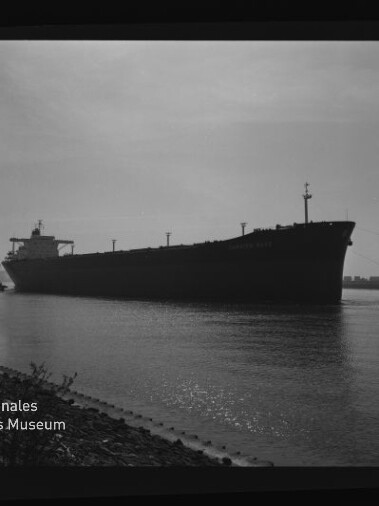 Große Schiffssilhouette (Frachtschiff/Tanker) auf ruhigem Wasser nahe Ufer, mit Wasserzeichen Internationales Maritimes Museum Hamburg.