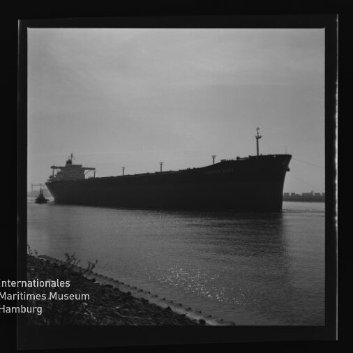 Große Schiffssilhouette (Frachtschiff/Tanker) auf ruhigem Wasser nahe Ufer, mit Wasserzeichen Internationales Maritimes Museum Hamburg.